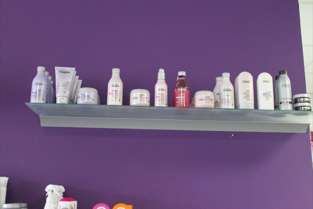 Een schap met flessen en potten van L'Oréal Professionnel tegen de paarse muur van de salon.